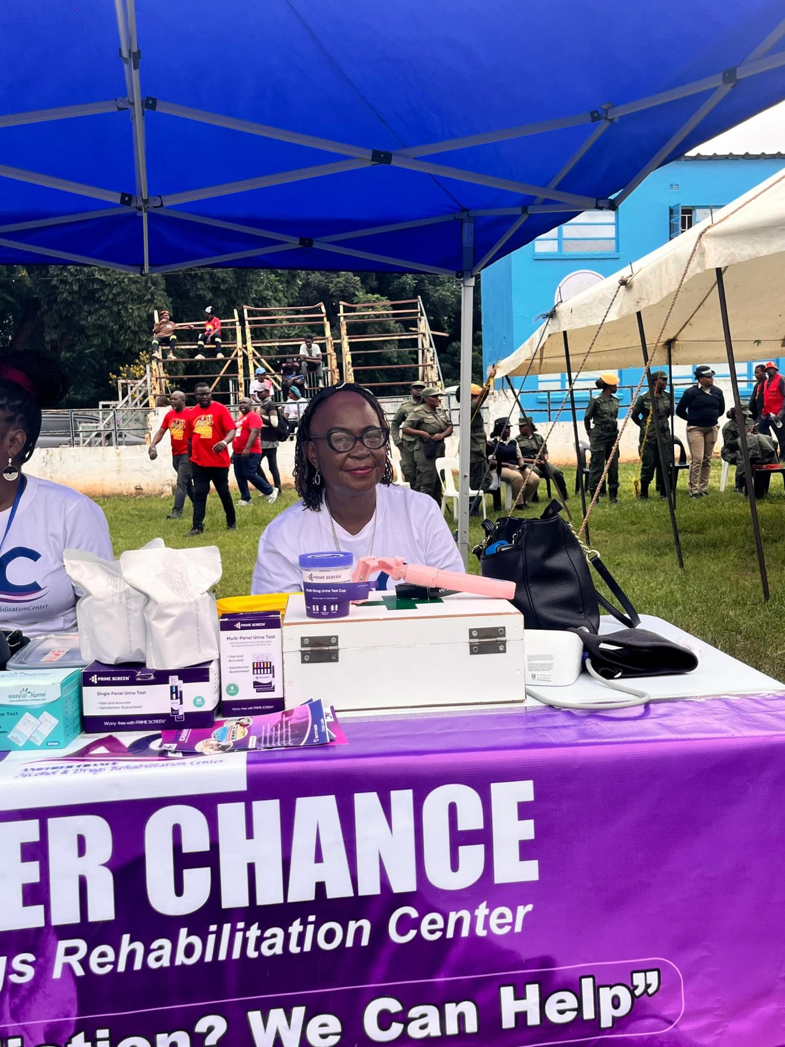 A staff member seated at an on-site screening and information desk under a tent
